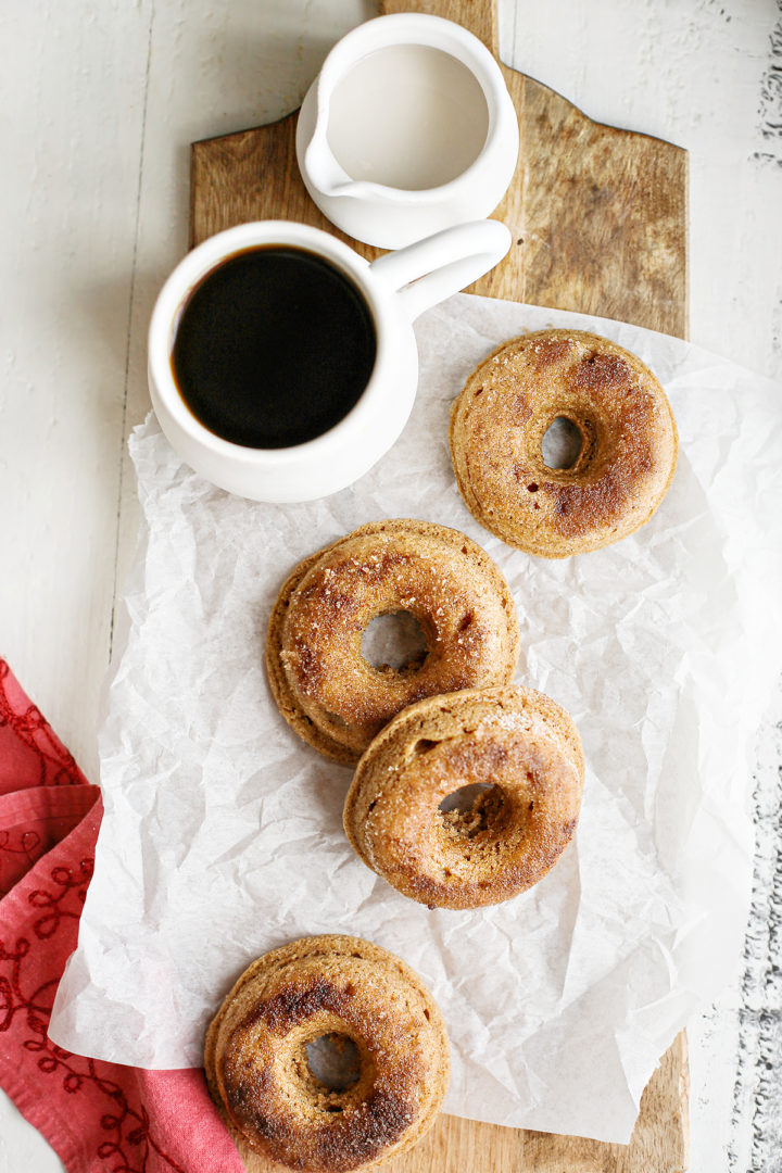 overhead photo showing the finished product of this baked donuts recipe - four baked cinnamon donuts next to a mug of coffee