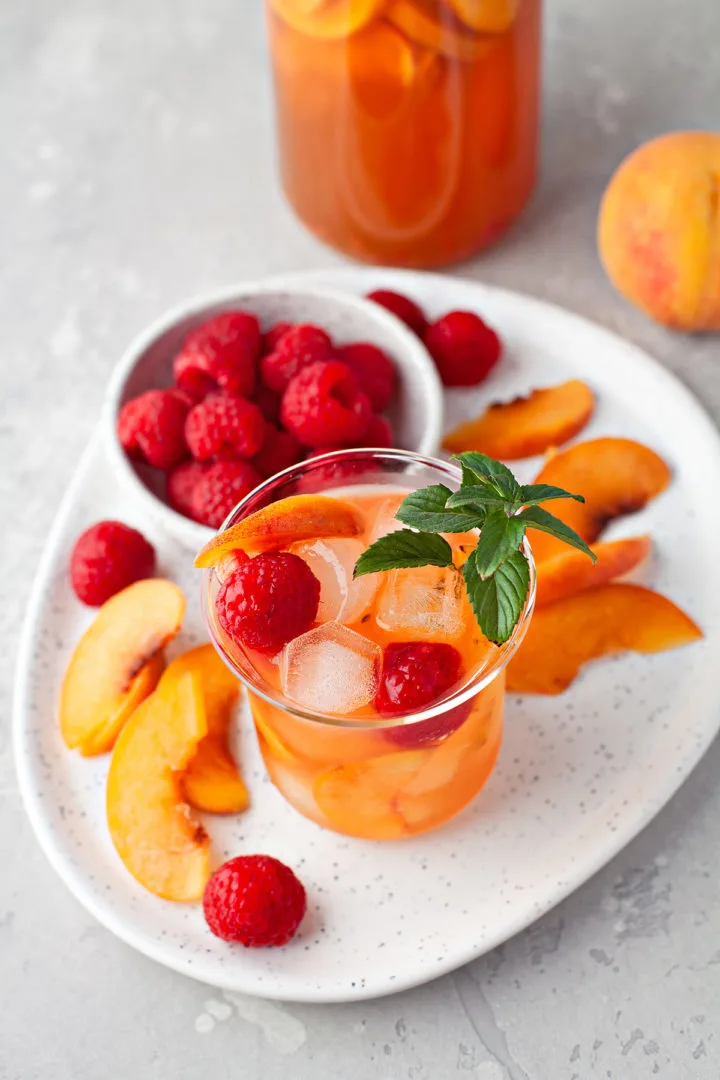 photo of a summer cocktail of peach sangria in a glass with raspberry and fresh mint garnish
