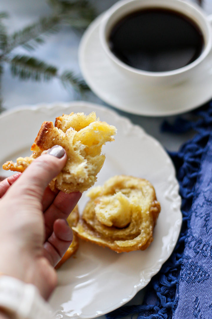 photo of a woman eating pecan sticky buns that are on a white plate next to a mug of coffee