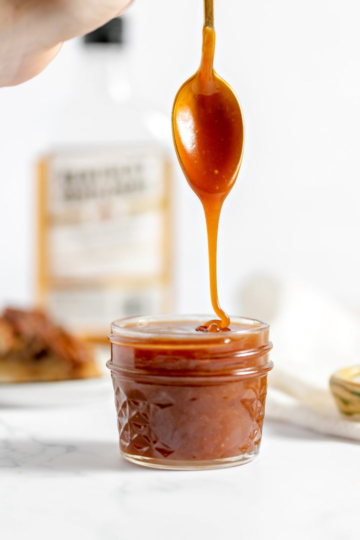 photo of rum caramel sauce drizzling off a spoon into in a jar full of caramel