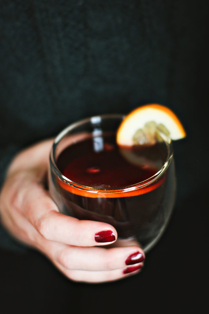 a woman holding a glass of hot spiced apple cider