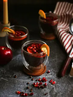 photo of glasses of spiced apple cider on a dark table with a candle