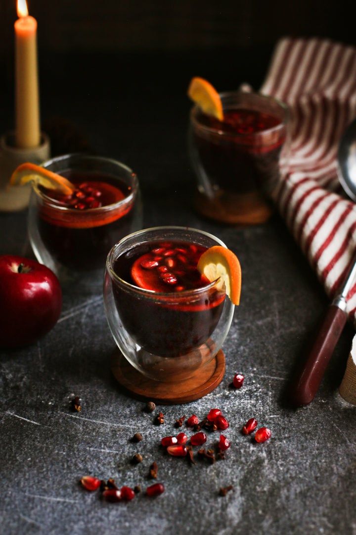 photo of 3 glasses of hot spiced apple cider on a dark table with a candle