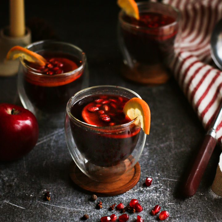 photo of glasses of spiced apple cider on a dark table with a candle