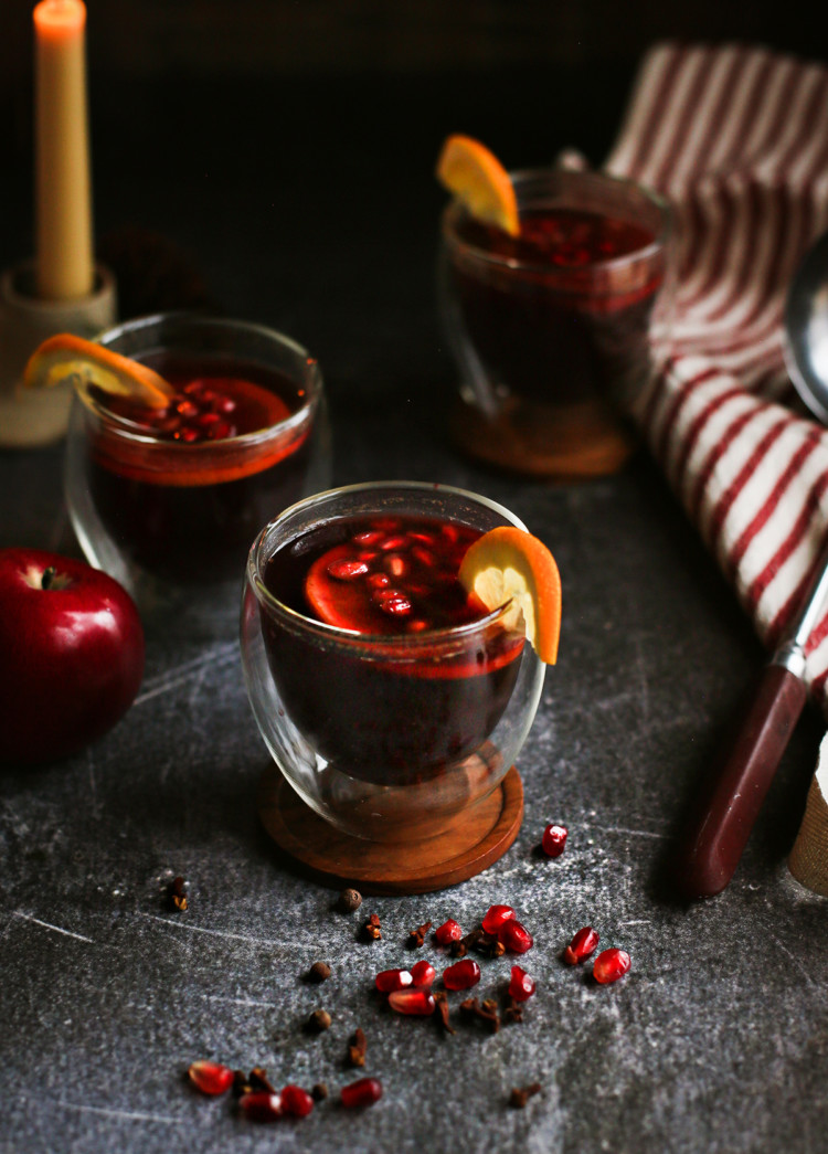 photo of glasses of spiced apple cider on a dark table with a candle