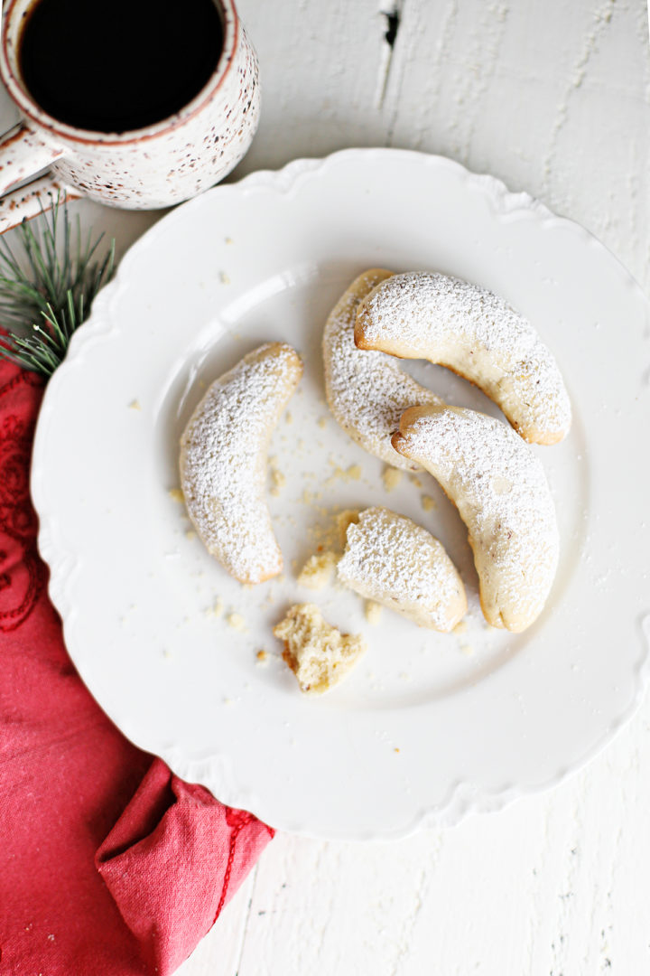 overhead photo of a plate of almond crescent cookies with a mug of coffee