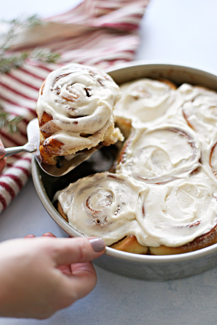 photo of a woman serving the best homemade cinnamon rolls from a baking pan