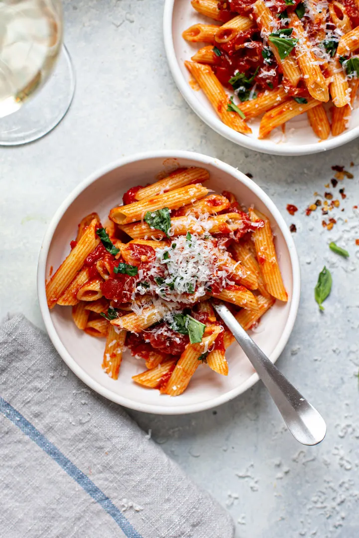 close up photo of pasta arrabbiata in a white bowl with a fork and a glass of wine