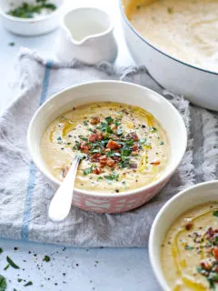 photo of a bowl of roasted cauliflower soup on the table next to a pot of cauliflower soup