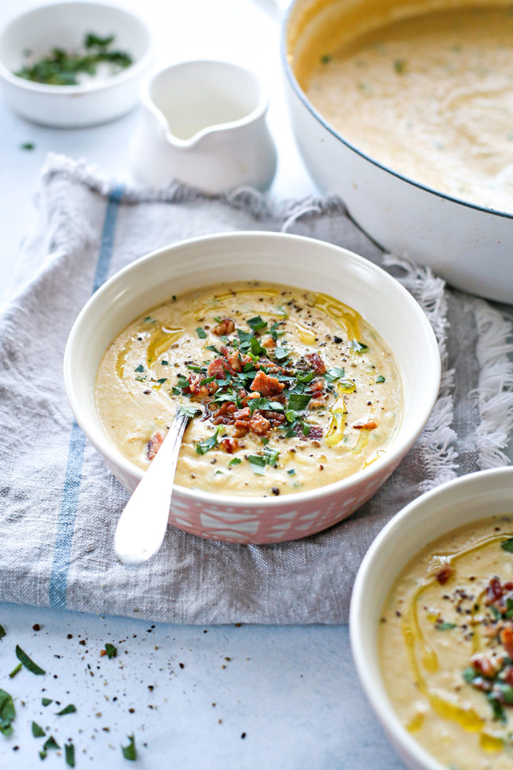 photo of a bowl of roasted cauliflower soup on the table next to a pot of cauliflower soup