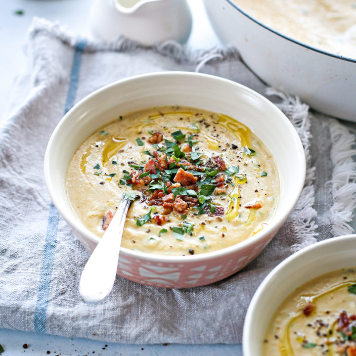 photo of a bowl of roasted cauliflower soup on the table next to a pot of cauliflower soup