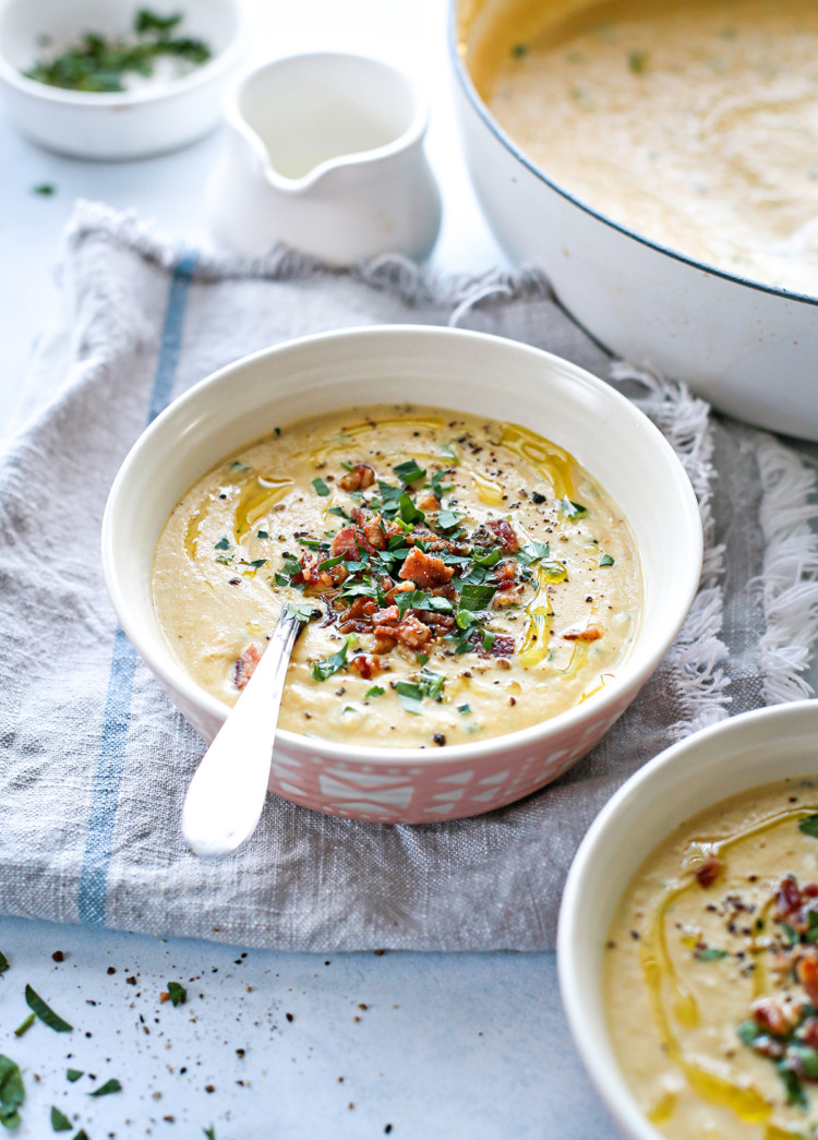 photo of a bowl of roasted cauliflower soup on the table next to a pot of cauliflower soup