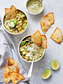 overhead photo of two bowls of chicken verde chili on a counter with tortilla chips and limes