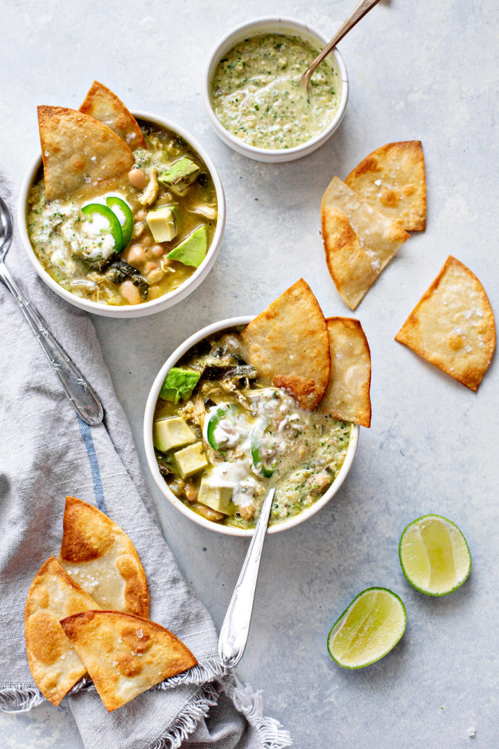 photo of two bowls of chicken chili verde with tortilla chips and spoons