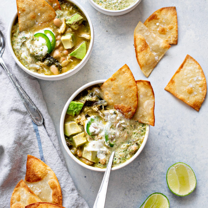 overhead photo of two bowls of chicken verde chili on a counter with tortilla chips and limes