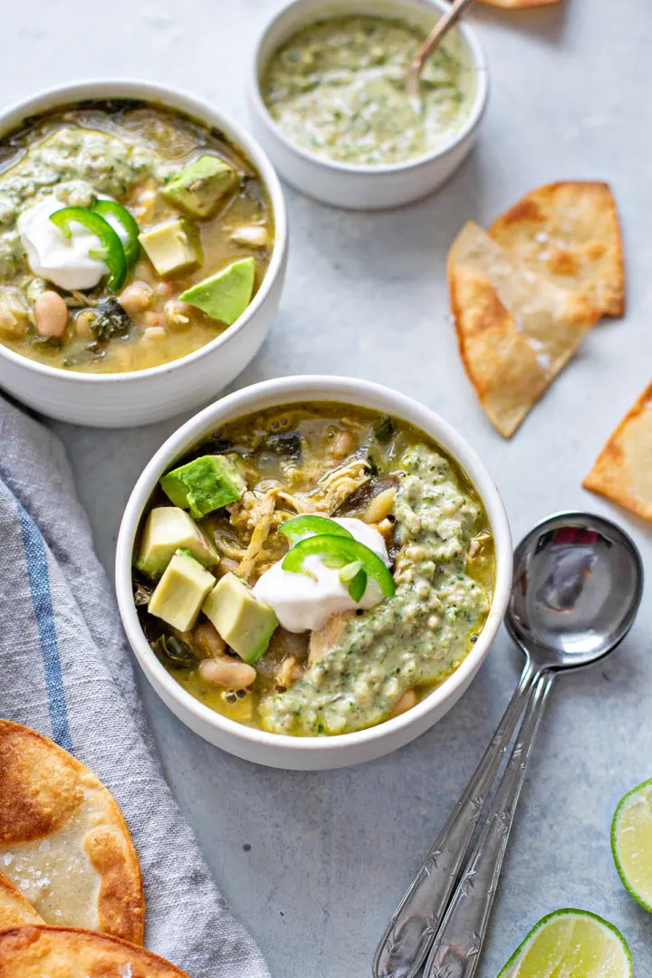 bowls of verde chicken chili topped with avocado and sour cream