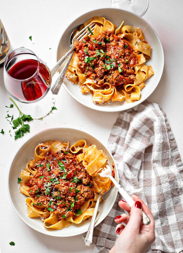 a table set with a glasses of wine and bowls of homemade bolognese sauce and pasta 