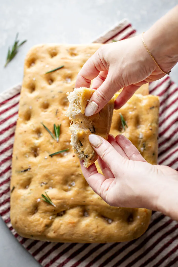 photo of woman eating a piece of focaccia bread with rosemary