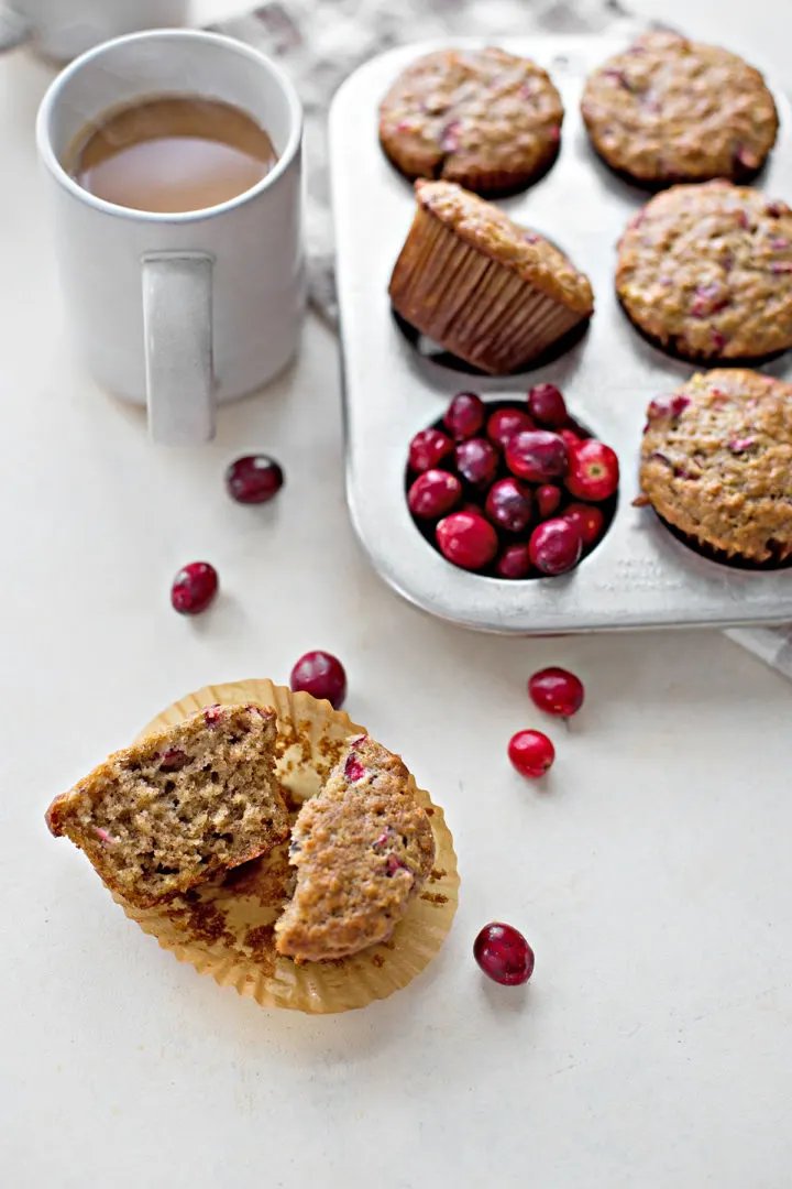 a cranberry muffin cut in half next to a coffee cup