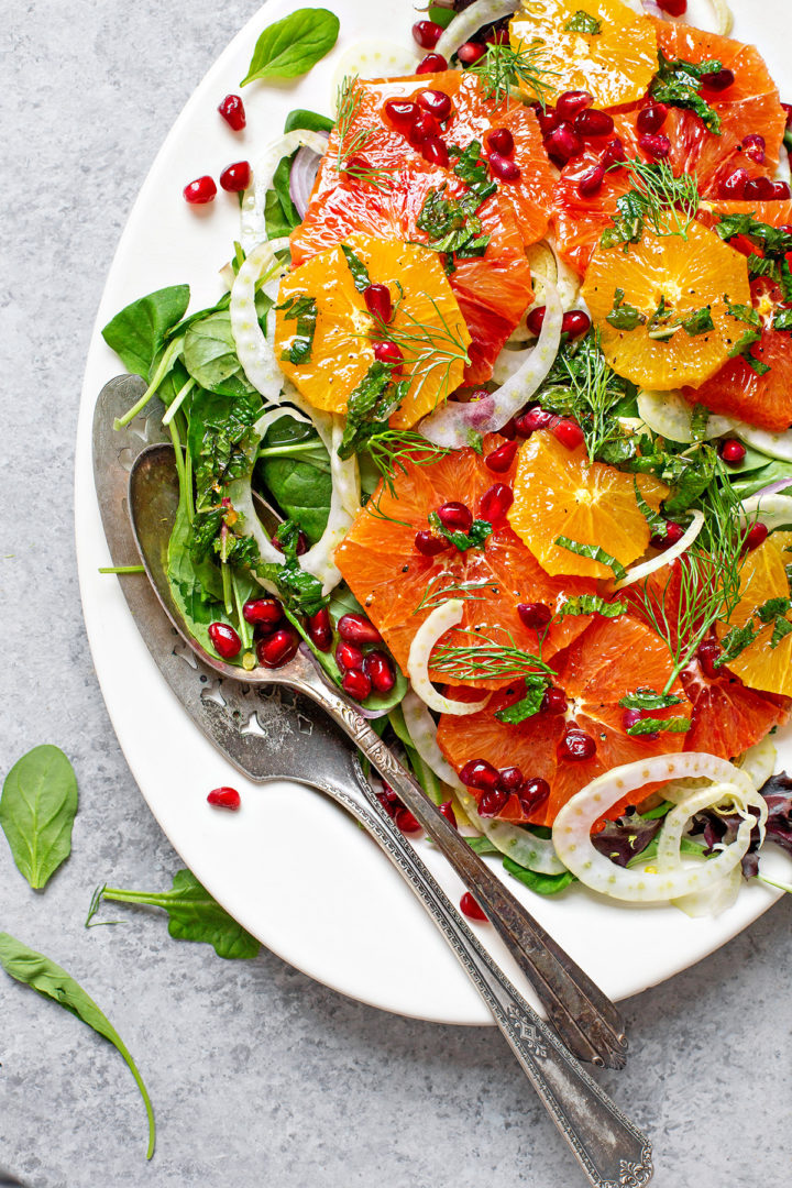 fennel salad with oranges and pomegranate on a white platter with serving utensils