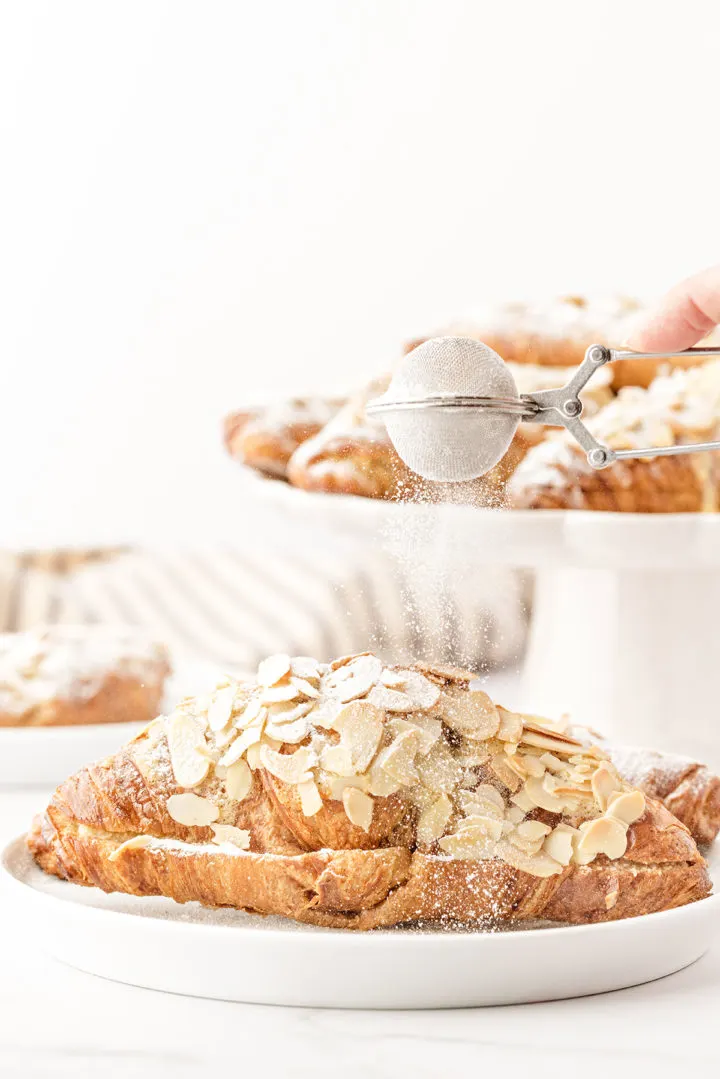 photo of a woman dusting powdered sugar on almond croissants