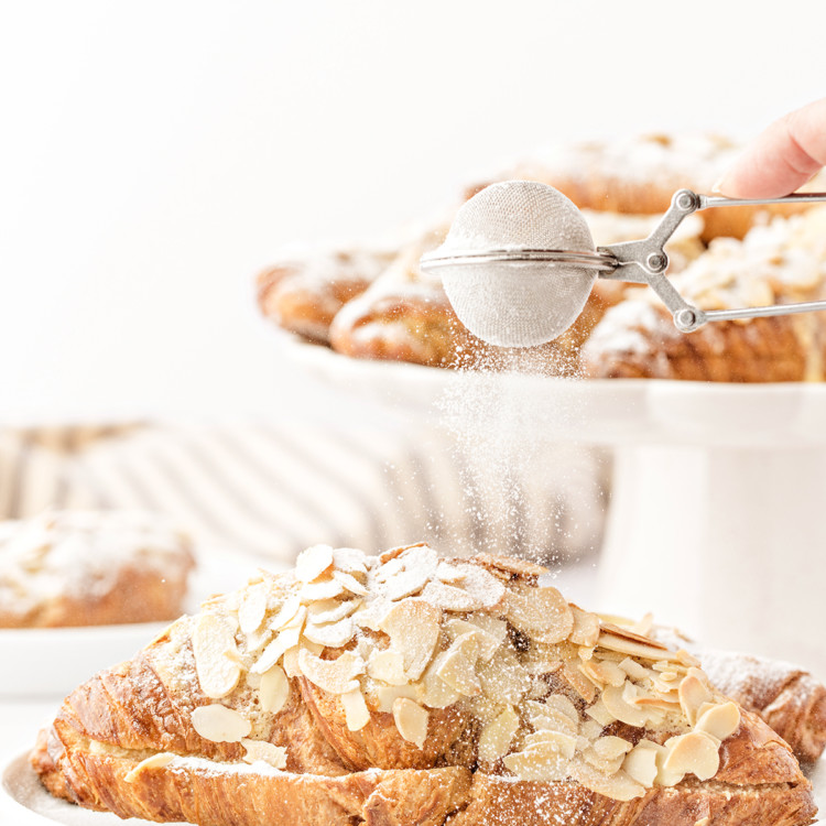photo of this recipe for almond croissants being dusted with powdered sugar