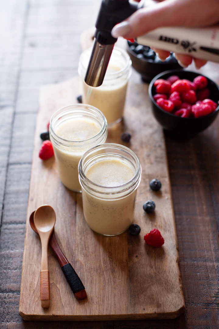 photo of jars of vanilla bean creme brulee with sugar on top being torched with a kitchen torch