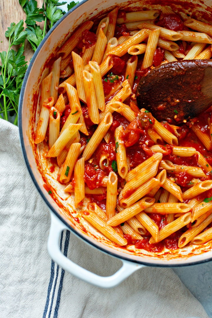 photo of arrabbiata sauce being mixed with penne pasta in a large pot