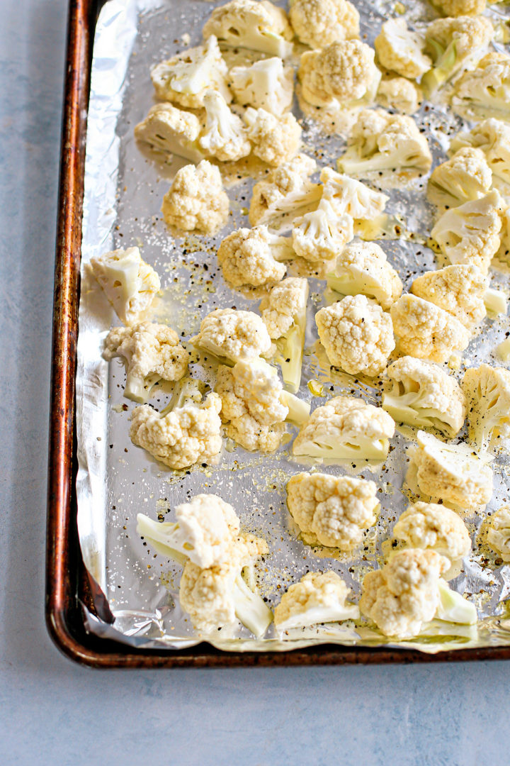 photo of cauliflower florets with olive oil, salt, and pepper on a foil lined baking sheet to make roast cauliflower