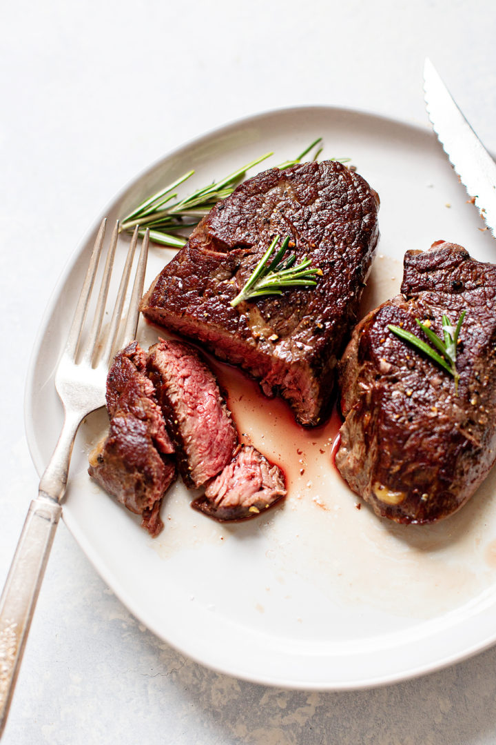 slices of sous vide steak on a white plate sitting next to a sprig of rosemary