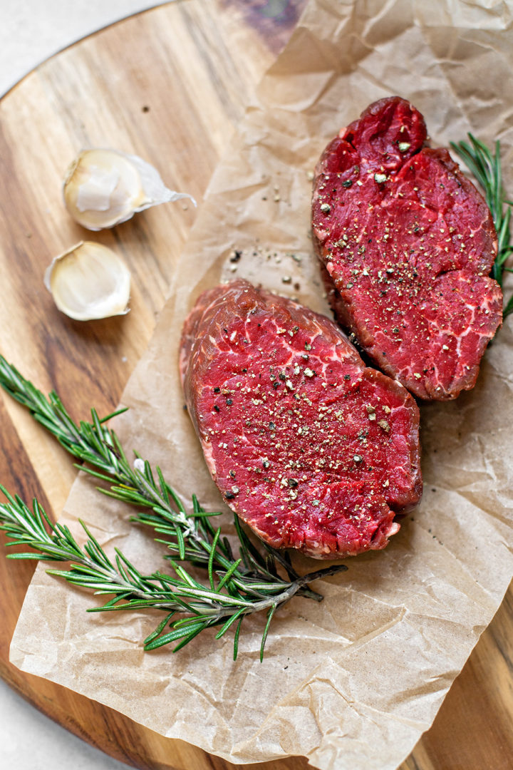 ingredients in this sous vide steak recipe(filet mingnon, salt, pepper, garlic, rosemary) sitting on a wooden cutting board