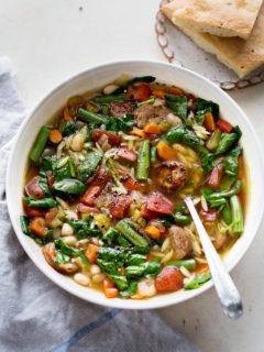 a white bowl filled with italian sausage soup with orzo