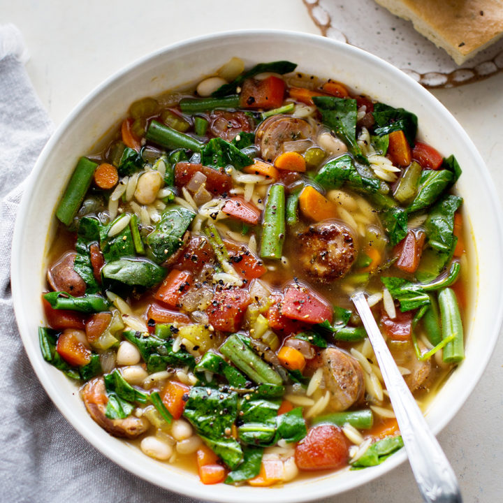 a white bowl filled with italian sausage soup with orzo