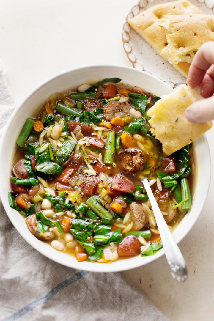 woman dipping focaccia bread into a bowl of this italian sausage soup recipe