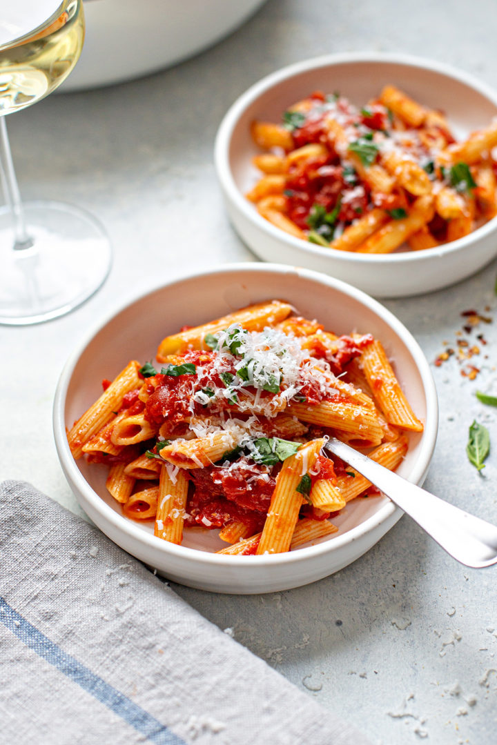 penne all’arrabbiata in white pasta bowls next to a glass of wine