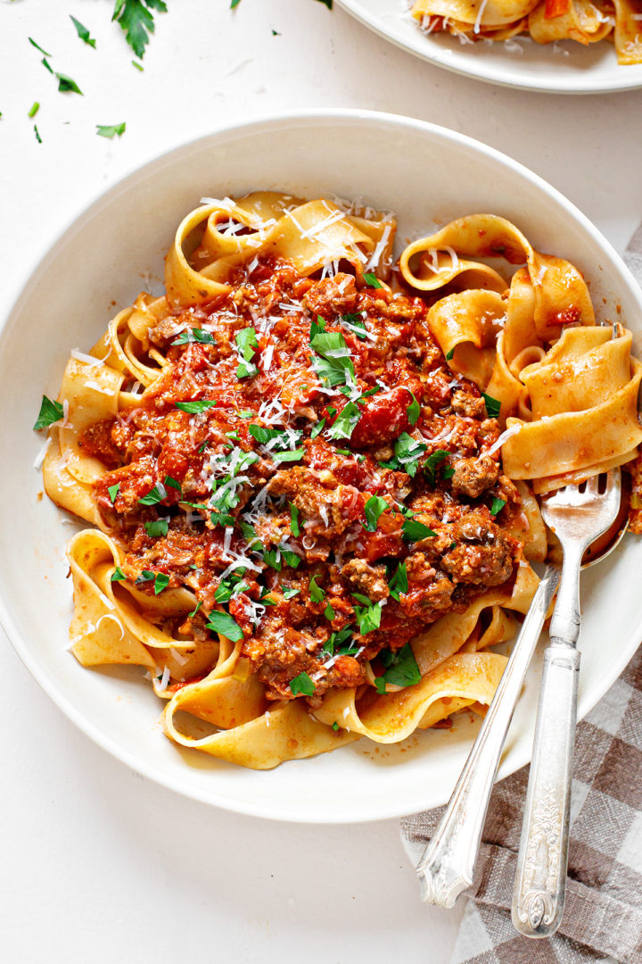 overhead close up photo of pasta bolognese in a white pasta bowl with a spoon and fork