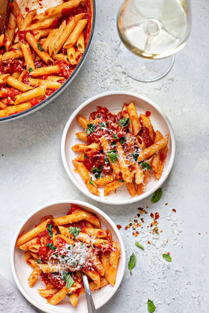 two bowls of penne pasta with arrabiata sauce, parmesan, and fresh basil on top