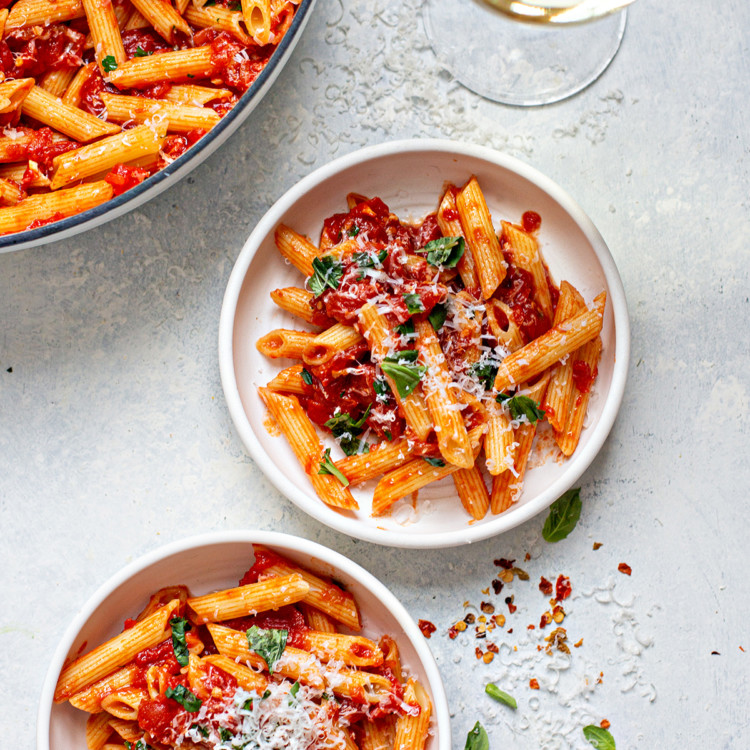 two plates of penne arrabbiata and a glass of wine