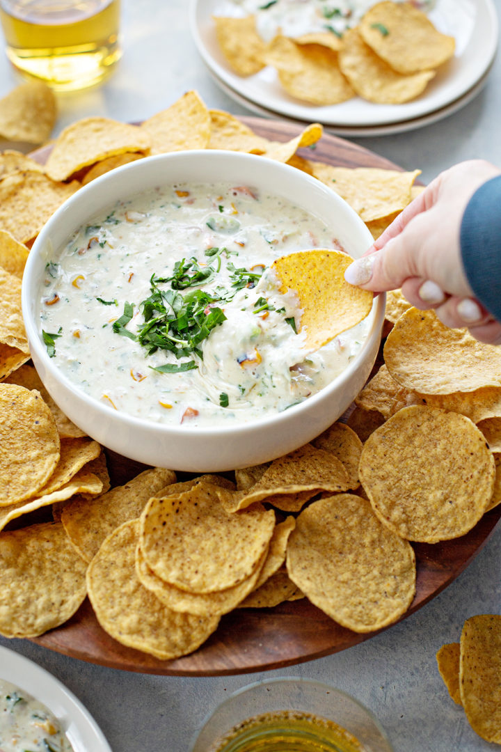 woman scooping chips in a bowl of the best white queso recipe