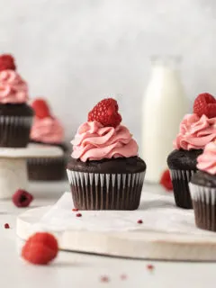 photo of chocolate raspberry cupcakes with raspberry frosting on a wooden cutting board with a jug of milk