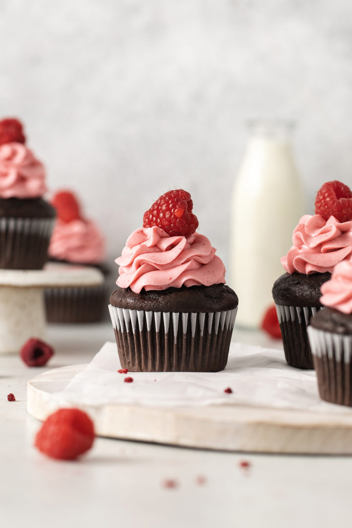 photo of chocolate raspberry cupcakes arranged on a white wooden cutting board with a pitcher of milk
