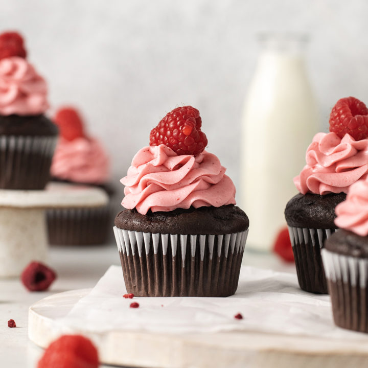 photo of chocolate raspberry cupcakes with raspberry frosting on a wooden cutting board with a jug of milk