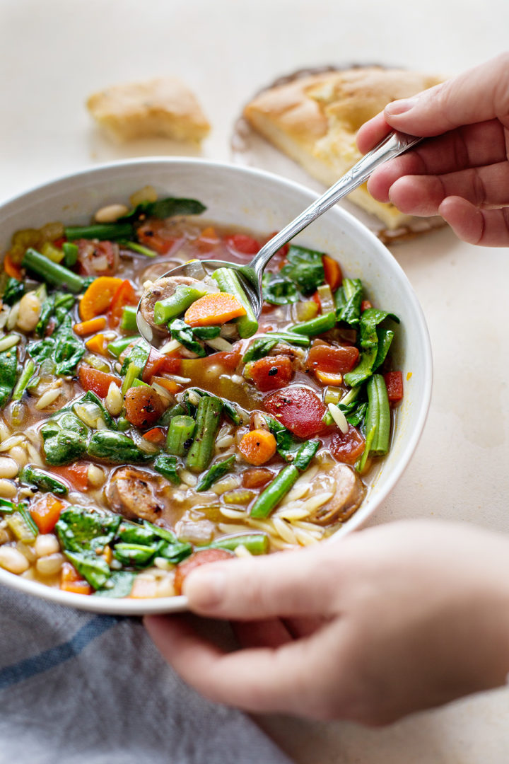 woman holding a bowl of italian sausage soup with orozo