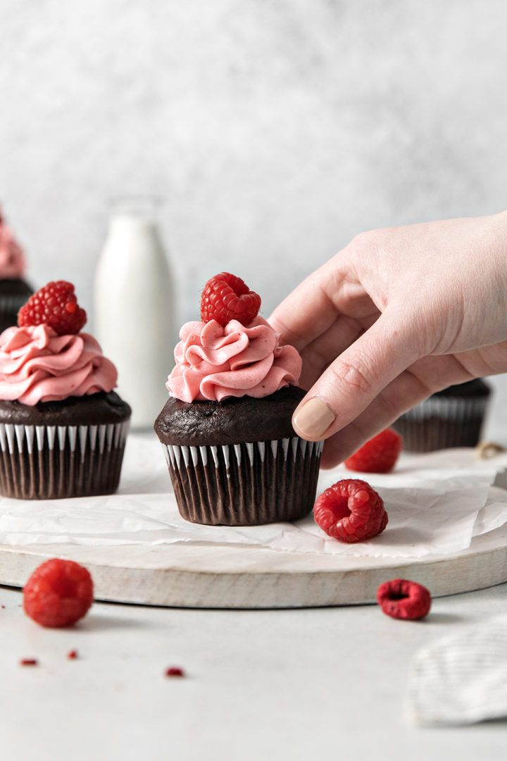 woman picking up a chocolate raspberry cupcake to eat