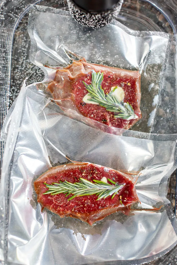 vacuum sealed filet mignon with rosemary and garlic cooking in a sous vide water bath