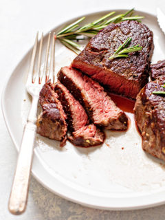 photo of a sous vide steak on a white plate with a fork, knife, and rosemary