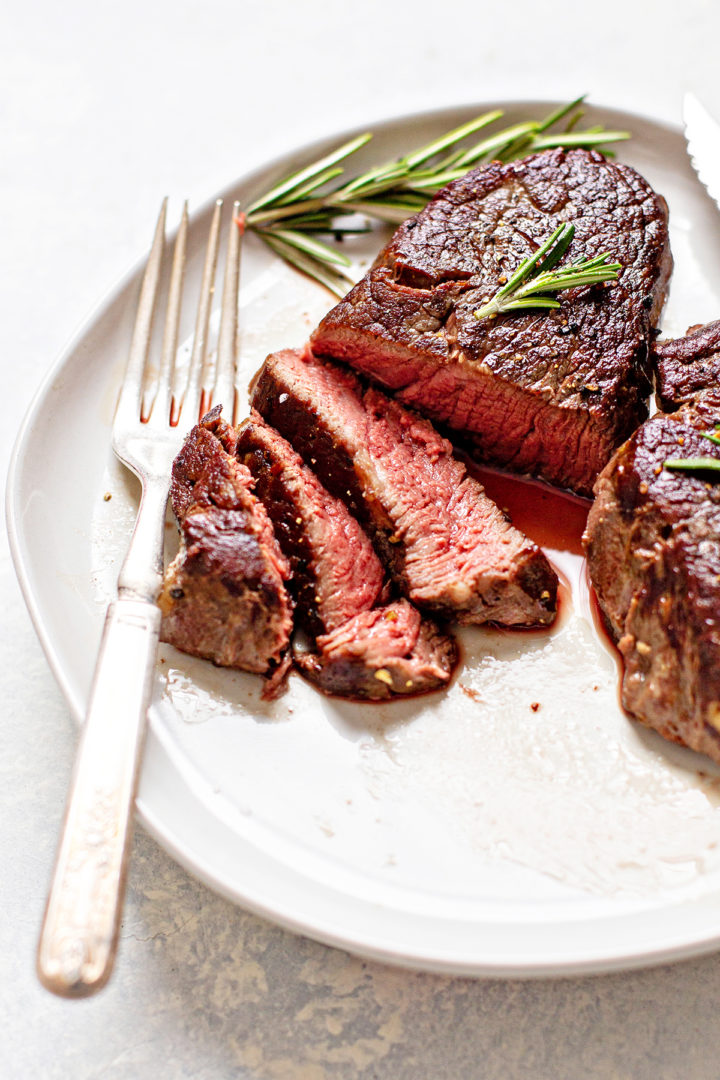 photo of a sous vide steak on a white plate with a fork, knife, and rosemary