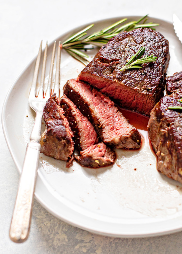 photo of a sous vide steak on a white plate with a fork, knife, and rosemary