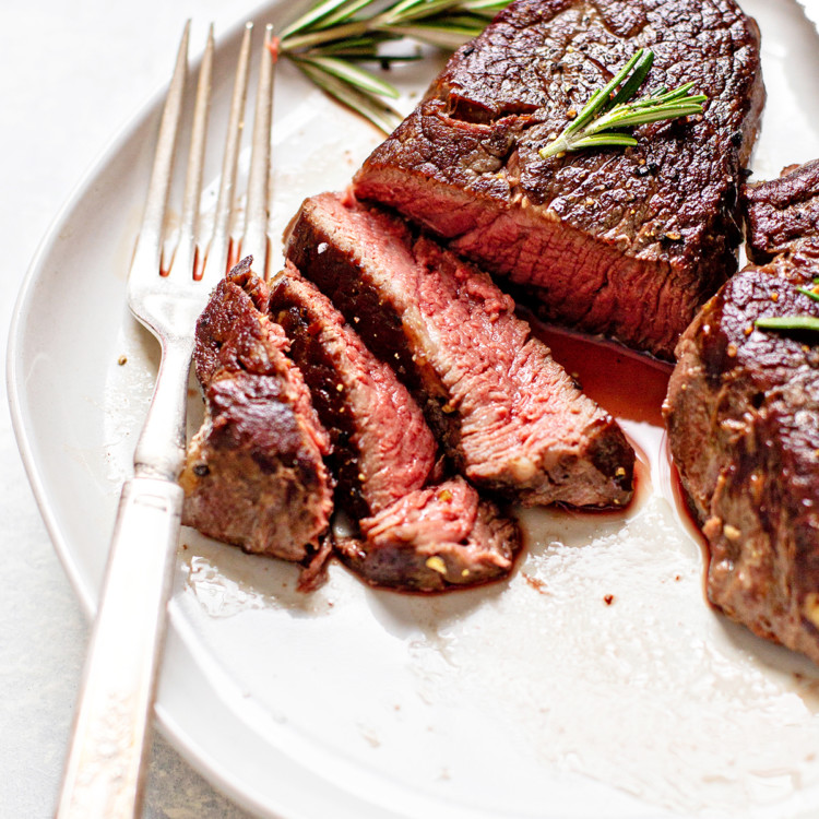 photo of a sous vide steak on a white plate with a fork, knife, and rosemary