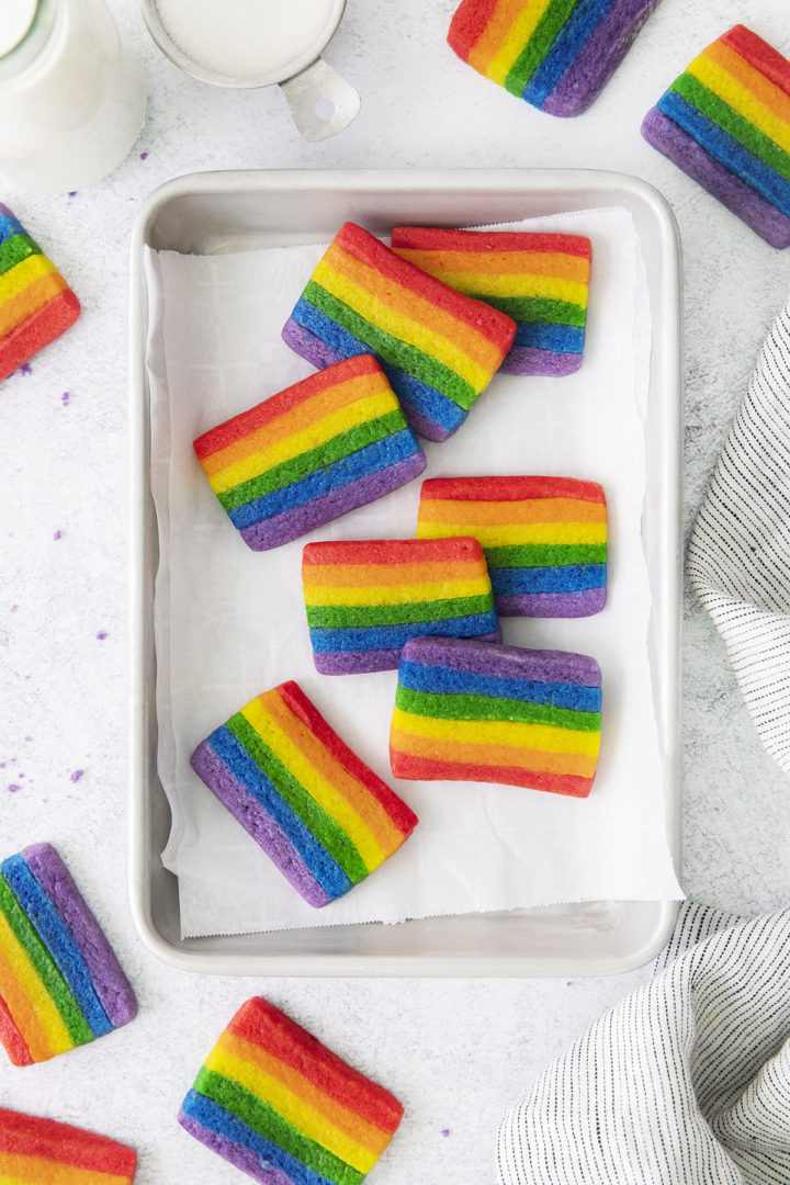 photo of a baking sheet with rainbow cookies on it next to a cup of milk